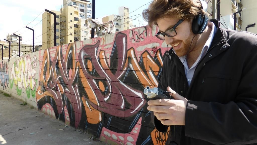 Young man with voice recorder standing in front of wall with graffiti
