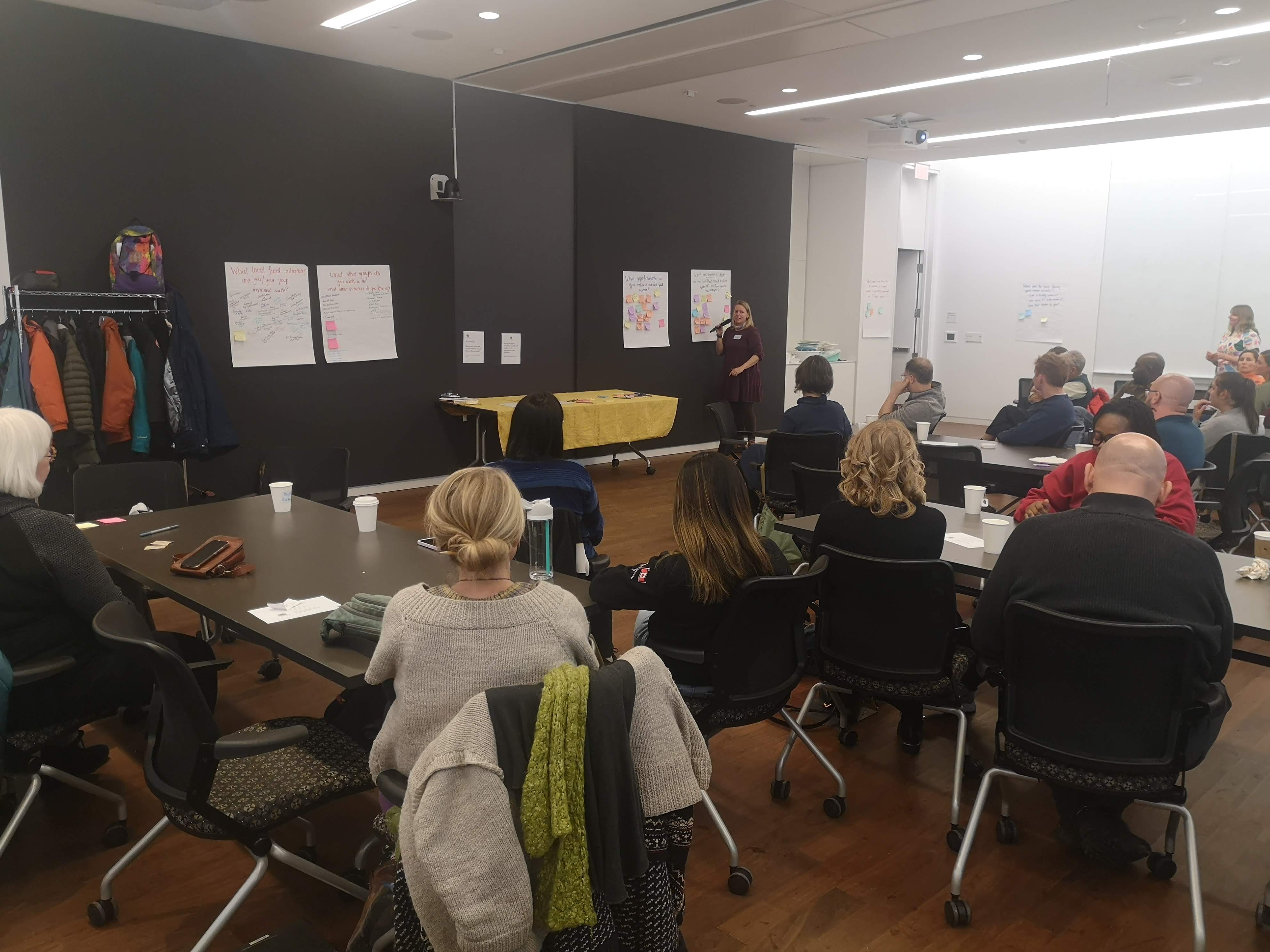 people gathered in a room listening to a speaker who is describing post-it notes on flip chart paper