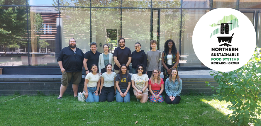 Group photo of students posing on grass with glass building in the background