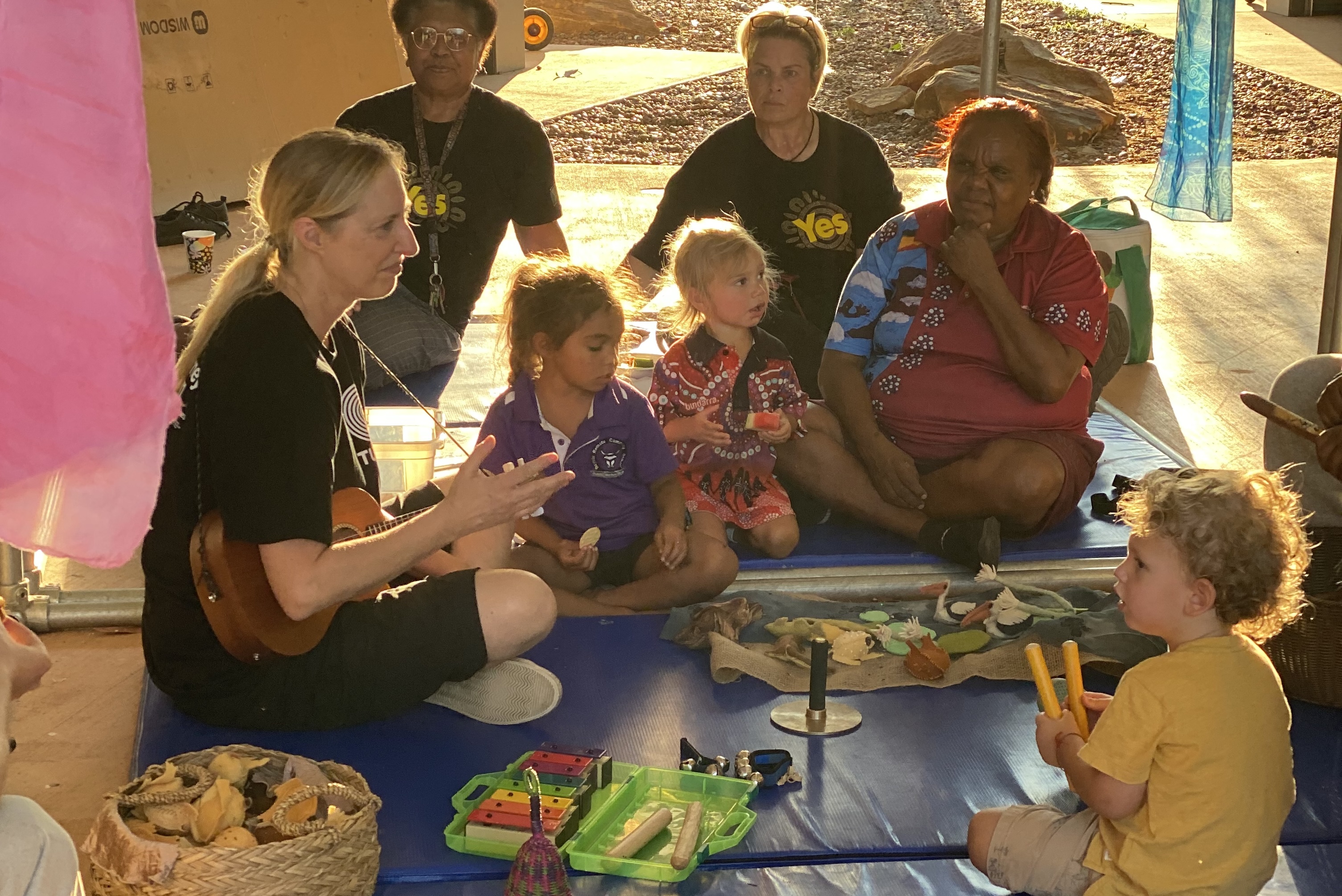 picture of Gillian Howell facilitating music outdoors on a mat with children and adults